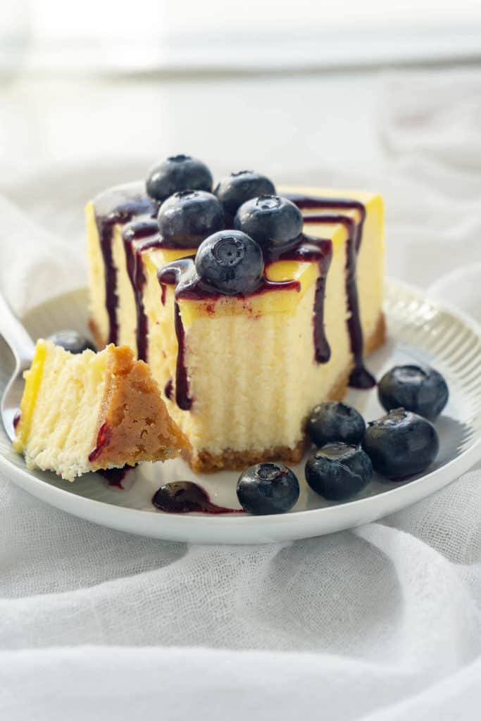 Luscious Lemon Blueberry Cheesecake - rich and creamy lemon cheesecake with a sweet shortbread crust, topped with lemon curd and a vibrant blueberry sauce. Melt-in-your-mouth creaminess and silky smooth. Pure deliciousness!