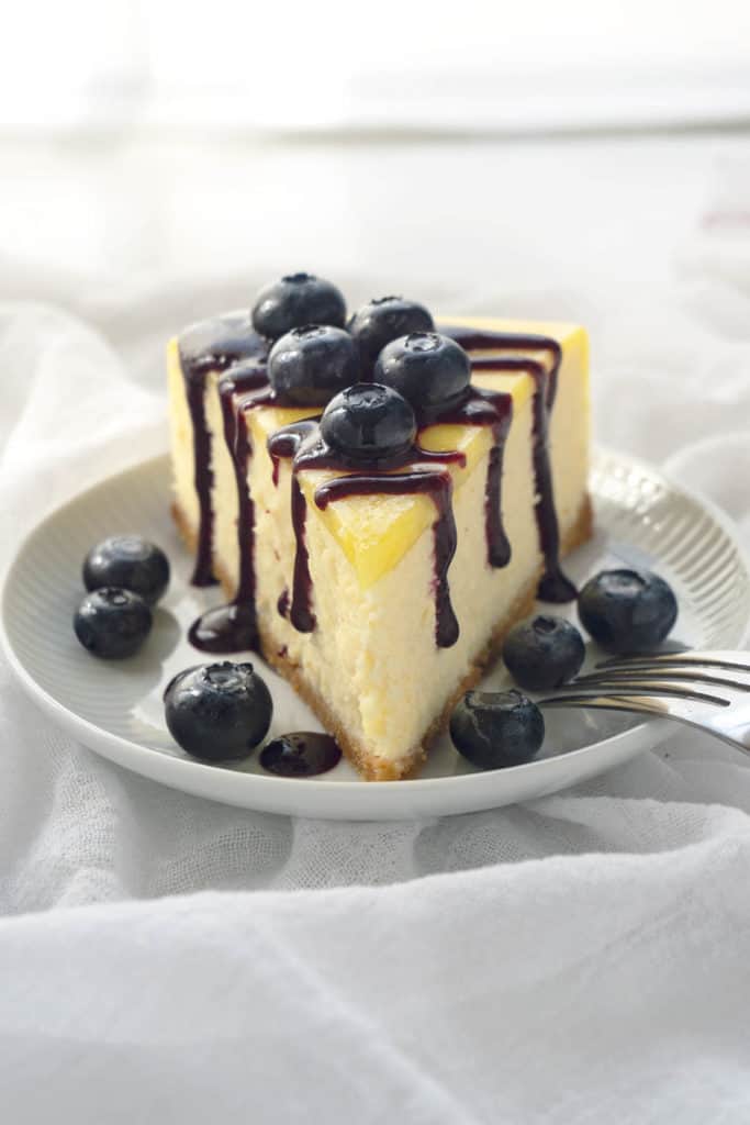 Luscious Lemon Blueberry Cheesecake - rich and creamy lemon cheesecake with a sweet shortbread crust, topped with lemon curd and a vibrant blueberry sauce. Melt-in-your-mouth creaminess and silky smooth. Pure deliciousness!