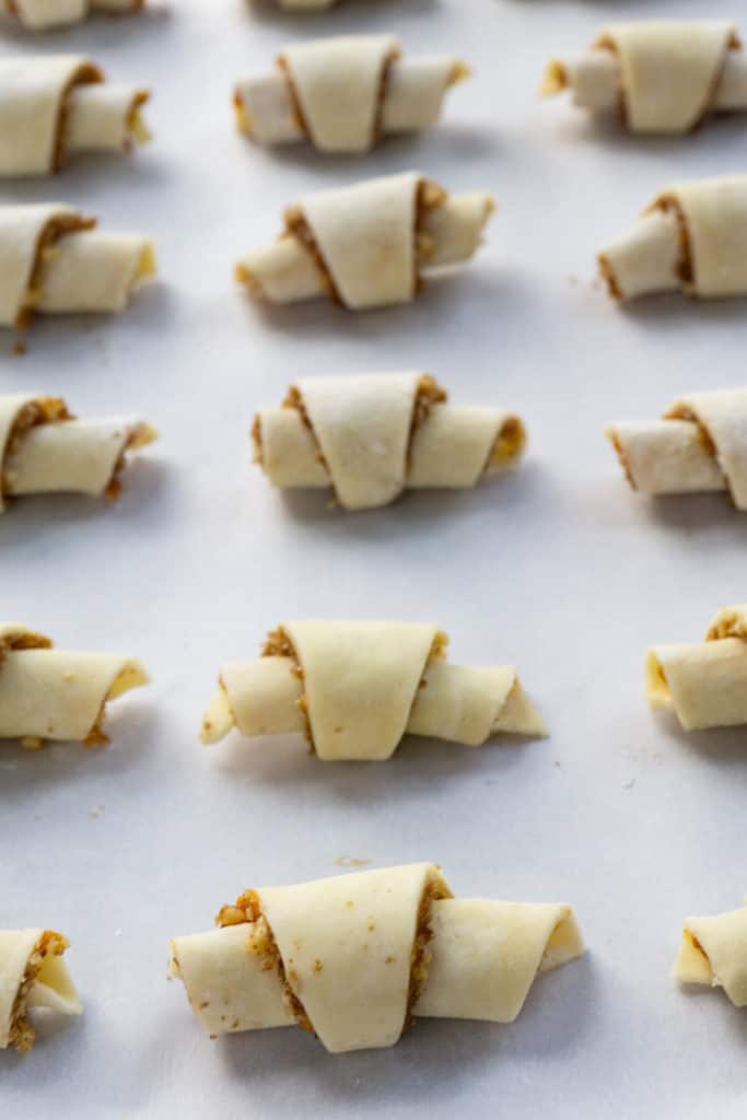 Rugelach, tiny crescent shaped pastries, are afamily favorite. A tender, flaky, cream cheese dough is wrapped around afilling of apricot jam, brown sugar, and walnuts. #rugelach #cookies #cookierecipes #recipes #holidayrecipes #holidaydesserts #holidaycookies
