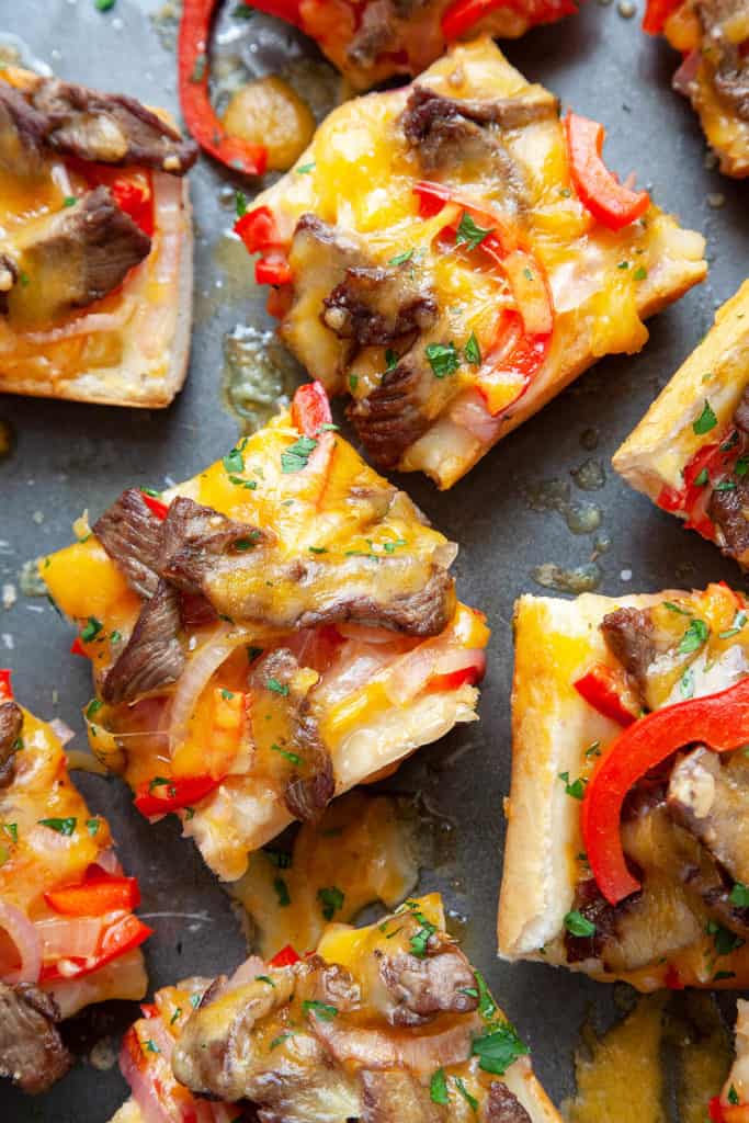 Melty cheese, strips of juicy steak, and sautéed peppers and onions, toasted on top of crusty French bread, this Cheesy Philly Cheesesteak Bread is a cross between a Philly Cheesesteak and a French bread pizza. Perfect for gameday, appetizer, snacking, or an easy dinner. Quick, easy, delicious. #phillycheesesteak #philly #cheesesteak #steak #pizza #frenchbread #cheese