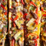 Melty cheese, strips of juicy steak, and sautéed peppers and onions, toasted on top of crusty French bread, this Cheesy Philly Cheesesteak Bread is a cross between a Philly Cheesesteak and a French bread pizza. Perfect for gameday, appetizer, snacking, or an easy dinner. Quick, easy, delicious. #phillycheesesteak #philly #cheesesteak #steak #pizza #frenchbread #cheese