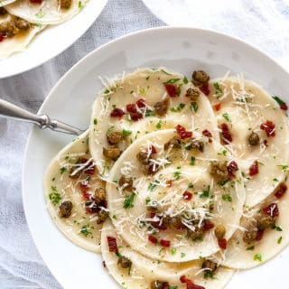 This Easy Artichoke Ravioli is full of the flavors of the Mediterranean! Ravioli is stuffed with lemony, marinated artichokes, creamy ricotta, and parmesan. It’s tossed in a simple parsley butter with sun dried tomatoes and fried capers sprinkled on top. Made quick and easy using dumpling wrappers (gyoza). #ravioli #pasta #gyoza #dumplingwrapper #wonton #italian #artichoke #sundriedtomato #capers #easy #dinner