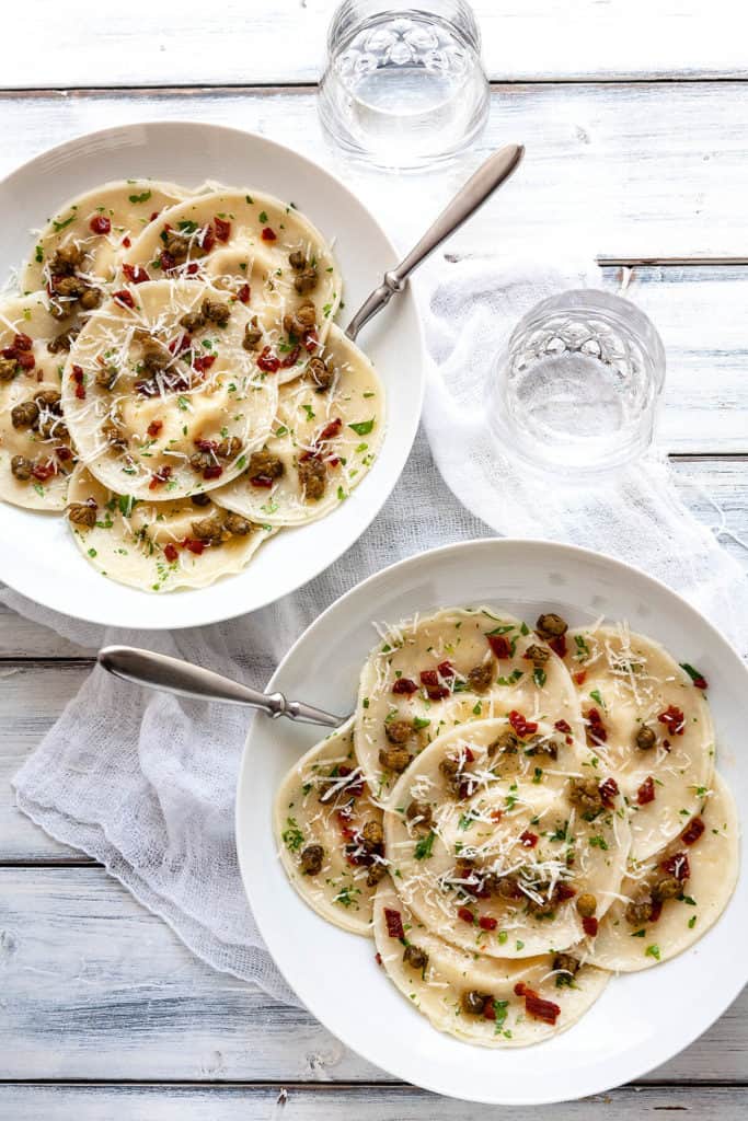 This Easy Artichoke Ravioli is full of the flavors of the Mediterranean! Ravioli is stuffed with lemony, marinated artichokes, creamy ricotta, and parmesan. It’s tossed in a simple parsley butter with sun dried tomatoes and fried capers sprinkled on top. Made quick and easy using dumpling wrappers (gyoza). #ravioli #pasta #gyoza #dumplingwrapper #wonton #italian #artichoke #sundriedtomato #capers #easy #dinner