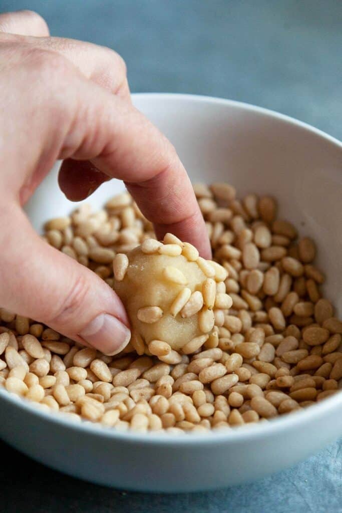 dipping a ball of Italian Pignoli Cookie dough into a bowl of pine nuts