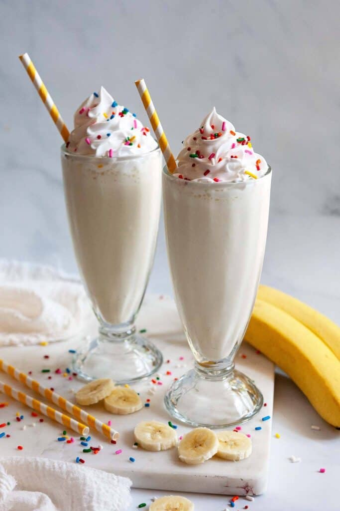 two banana milkshakes in old fashioned milkshake glasses topped with sprinkles