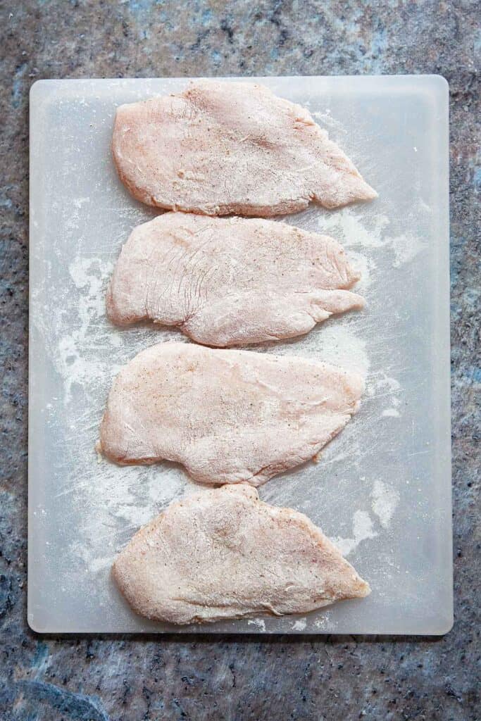 cutting board with chicken breasts dusted in flour