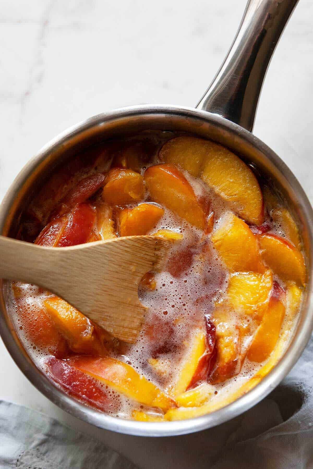 sliced peaches, sugar, and water cooking in a pan to make peach syrup
