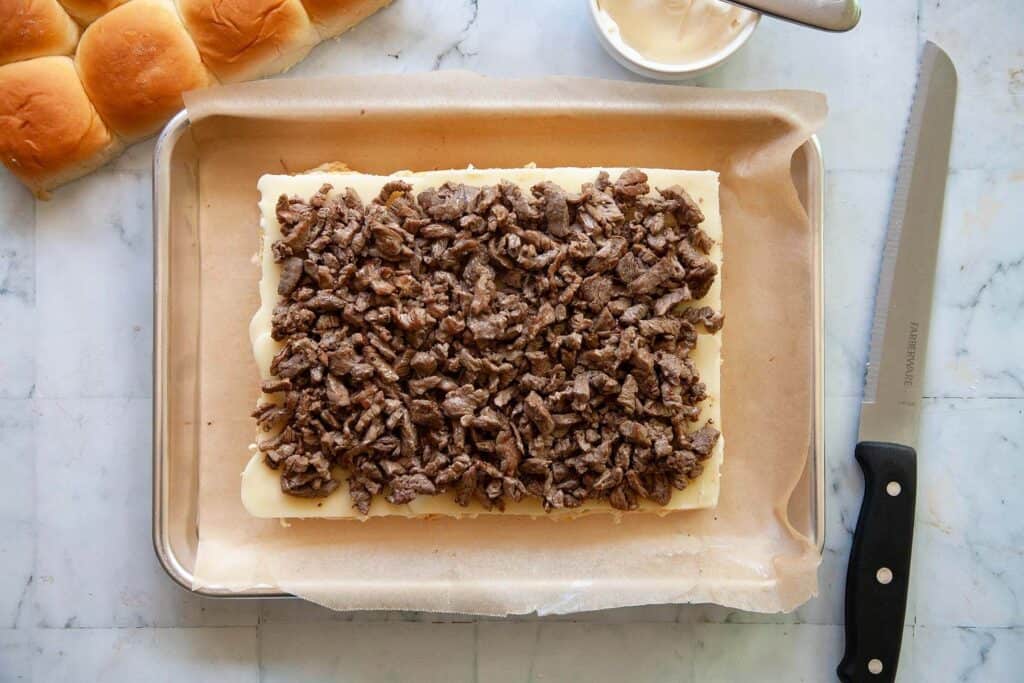 layering cooked steak on Philly Cheesesteak Sliders