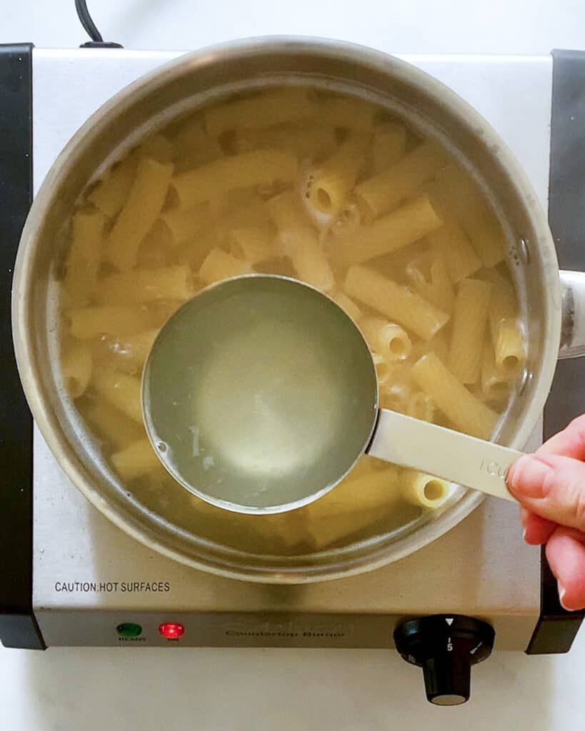 removing a cup of pasta water from the boiling pasta
