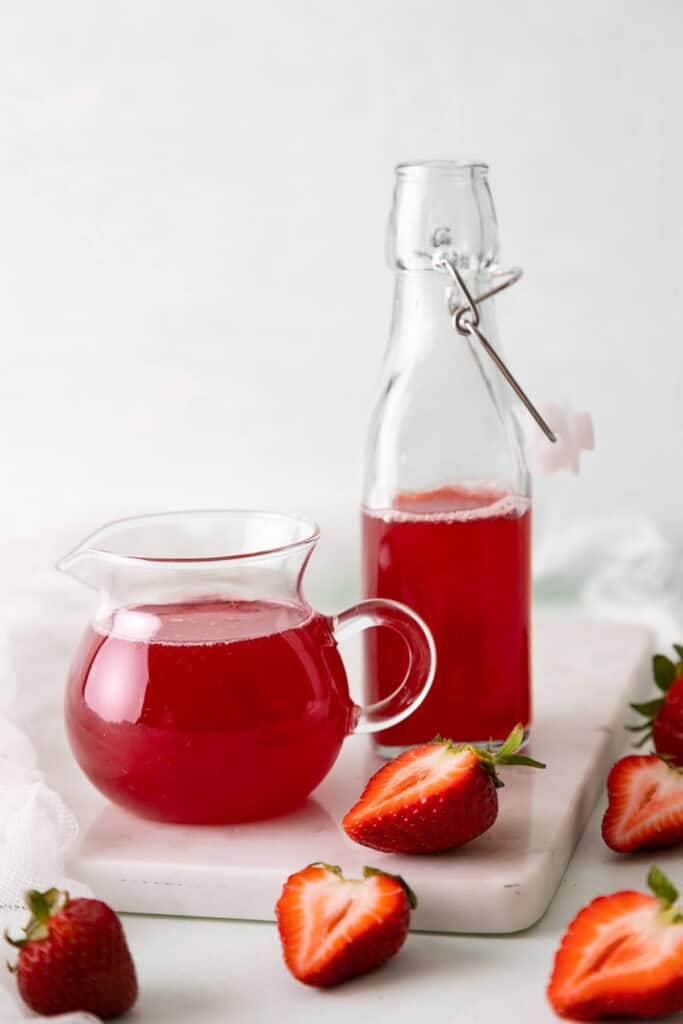 a small pitcher and bottle of strawberry syrup