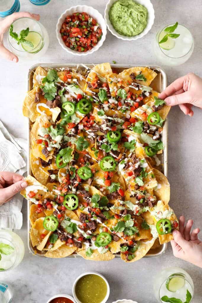 pan of carne asada nachos with hands picking up chips