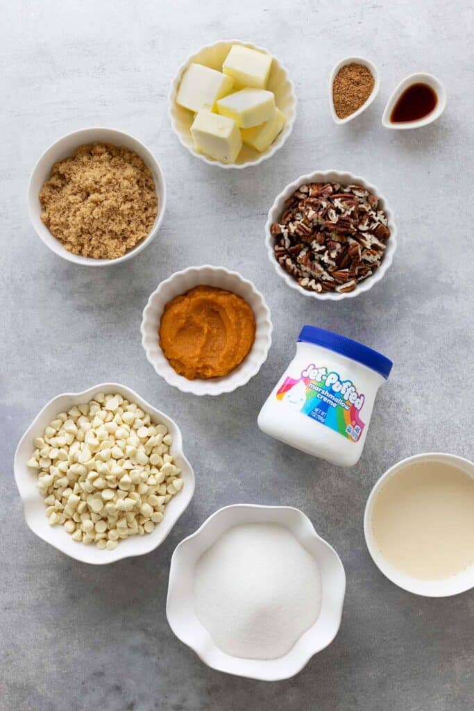 ingredients for pumpkin fudge in bowls: white chocolate chips, sugar, brown sugar, marshmallow creme, pumpkin, pecans, butter, and salt