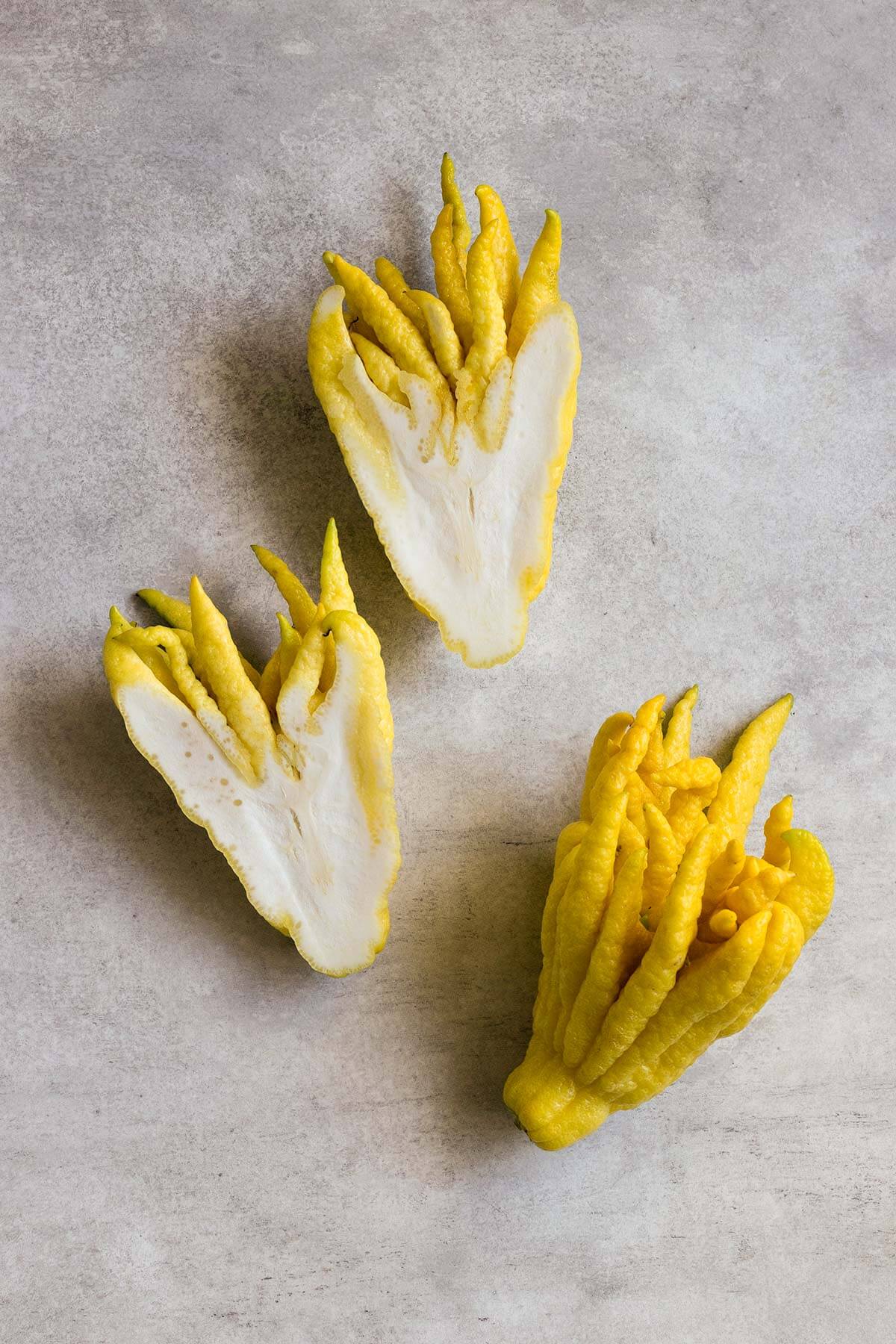 a photo of a buddha's hand citron fruit whole and cut in half showing the pithy interior