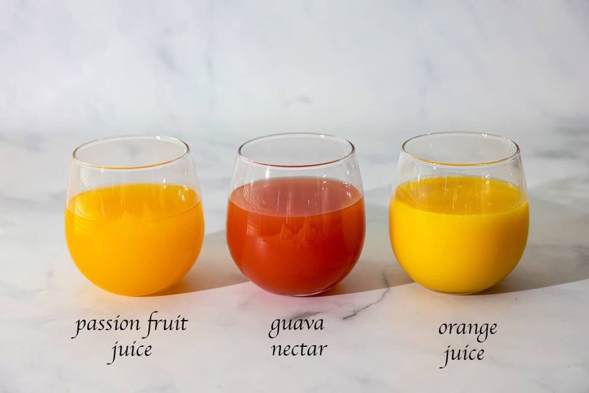 3 glasses of passion fruit juice, orange juice, guava juice on a counter