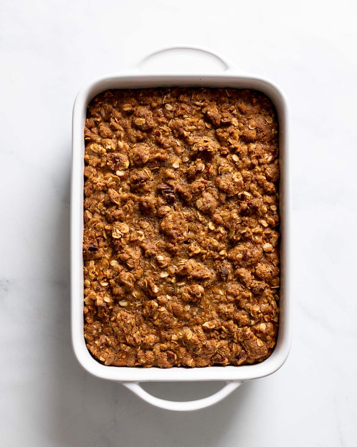 A freshly baked pumpkin crisp in a white baking dish, showing a golden-brown oat and pecan crumble topping.